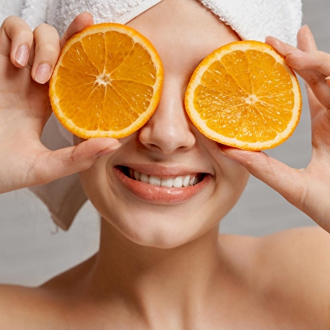 Moteris užsidengusi akis apelsinais, vienu iš pagrindinių AHA rūgščių- citrusiniu vaisiu. 